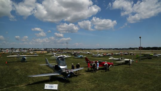 Attendees examining parked planes in a field at EAA AirVenture