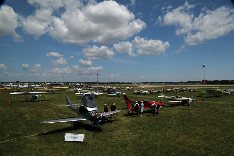Attendees examining parked planes in a field at EAA AirVenture