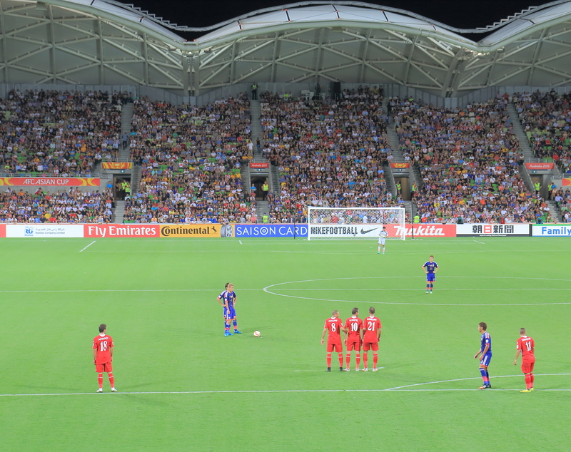 Two soccer teams competing in front of a packed stadium at the AFC Asian Cup.