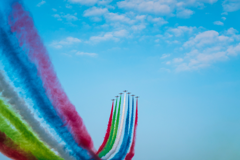 Jets flying in formation being trailed by green, blue, red, and white smoke at the Abu Dhabi Air Expo.