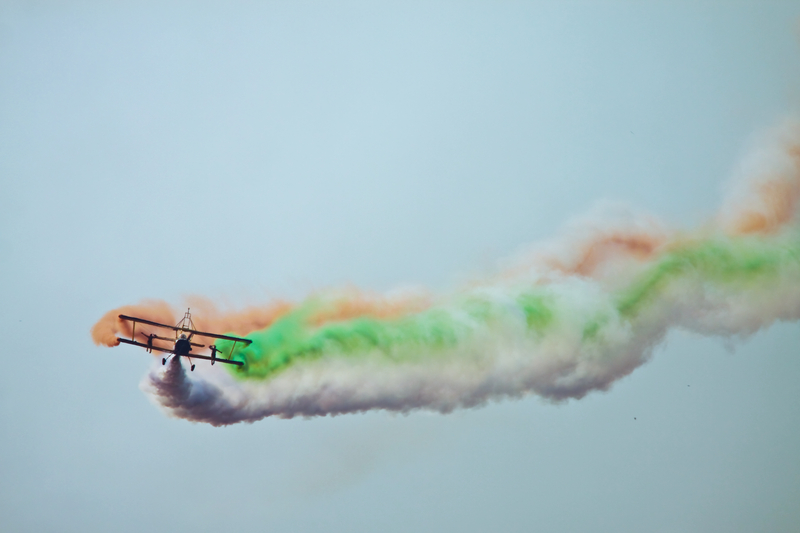 A biplane performing aerial stunt with red, green, and white smoke trailing at Aero India.