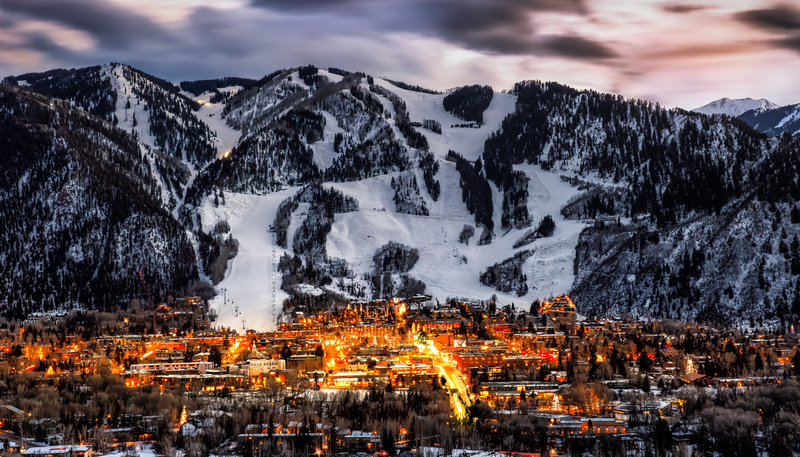 Snow covered mountains rising above the city of Aspen with all building lights on during the Aspen FilmFest.