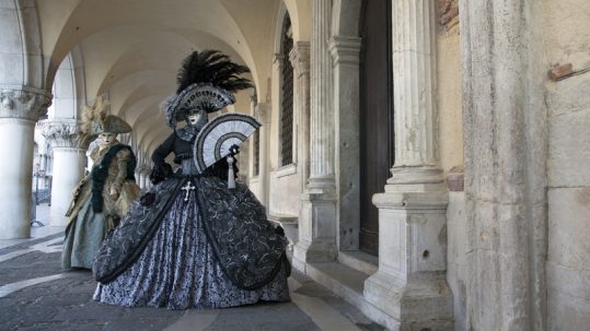 People in masks and elegant Victorian costumes at the Carnival of Venice.