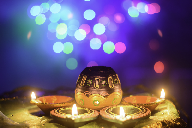 Diwali Diya lights in foreground with blurred colorful lighting in background.