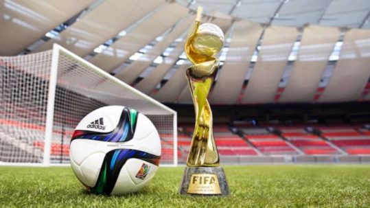 FIFA Women's World Cup Final trophy and soccer ball in front of a goal with an empty stadium as a backdrop.