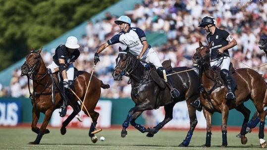 Riders and horses competing in front of spectators at the Hurlingham Open Polo Championship.