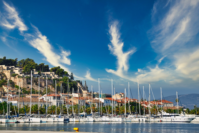 Yachts docked in the Nafplion Greece harbor with a picturesque cliff backdrop at the Mediterranean Yacht Show.