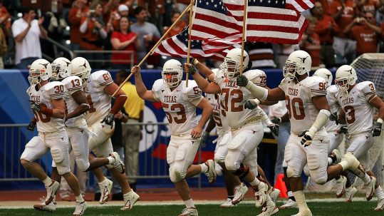 University of Texas football players running onto the field carrying American flags for the NCAA College Football Playoffs.