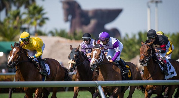 Horses with jockeys racing along the rail with a giant stone pegasus statue in the background at the Pegasus World Cup Invitational Stakes.