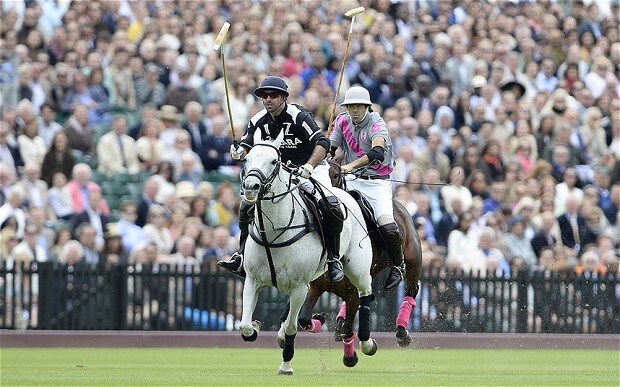 Two riders competing in front of a large crowd at the Queen's Cup Polo Championship.
