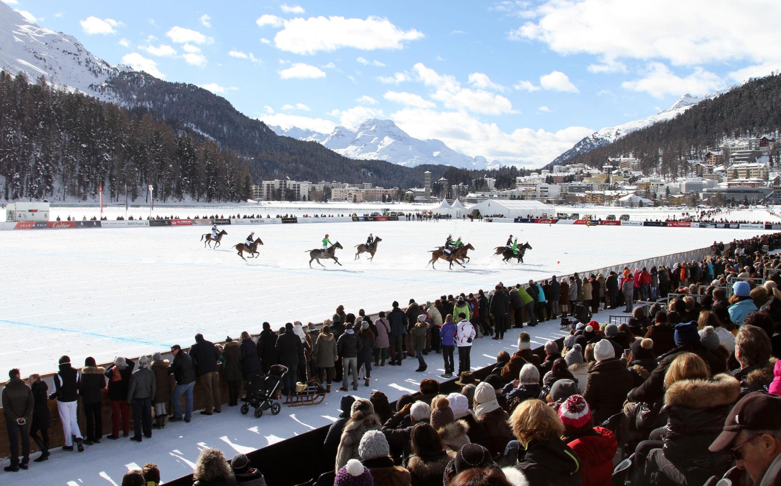 Spectators cheering as polo players compete on a snow-covered field at the Snow Polo World Cup.