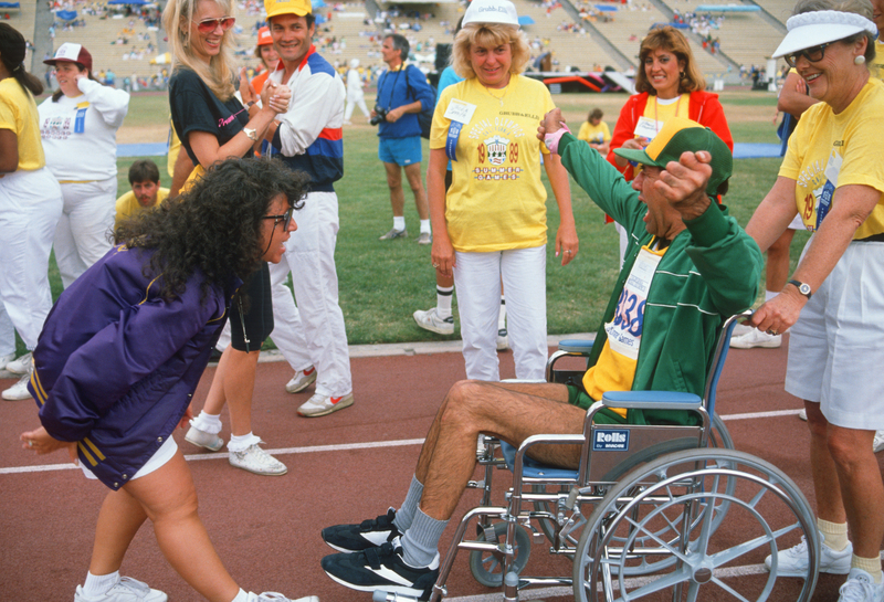 Athlete in wheelchair being encouraged by workers at the Special Olympics World Summer Games.