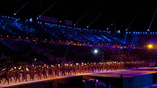 Athletes walking on the track in a stadium filled with spectators at night during the opening ceremony of the Special Olympics World Winter Games.