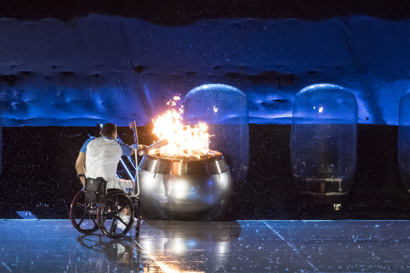 Athlete in wheelchair lighting the fiery cauldron with the torch for the Summer Paralympics.