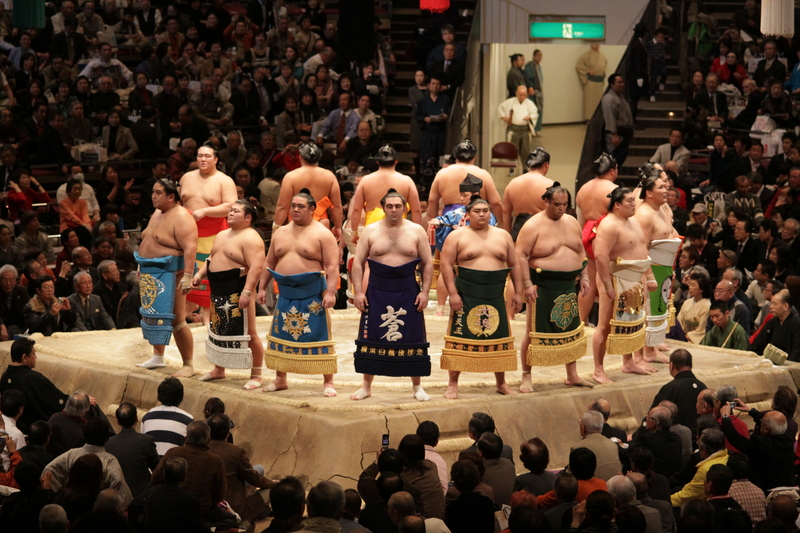 Several sumo wrestlers standing in a circle on the mat in front of spectators at the Sumo Grand Tournaments.