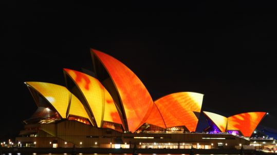 Sydney Opera House lit up with orange lights at night during Sydney Festival.