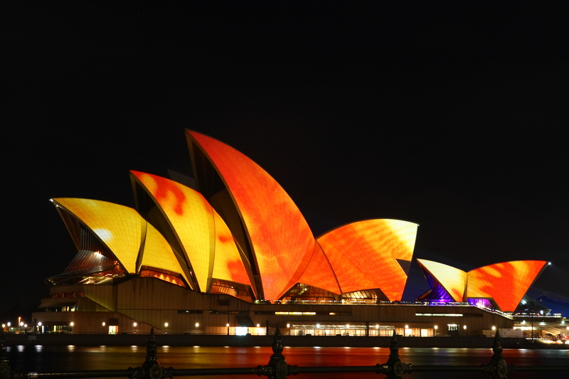 Sydney Opera House lit up with orange lights at night during Sydney Festival.