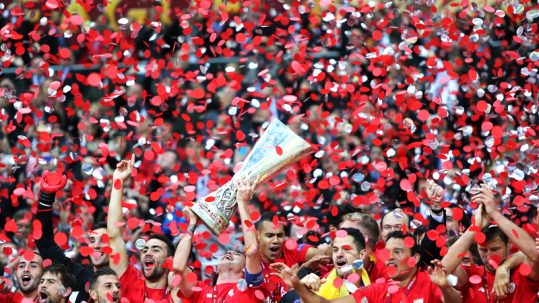 Team hoisting the trophy and celebrating while confetti rains down after winning the UEFA Europa League Final.