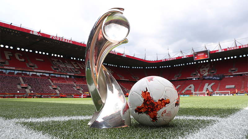 UEFA Women's Euro Cup trophy next to a soccer ball on the pitch of a stadium.