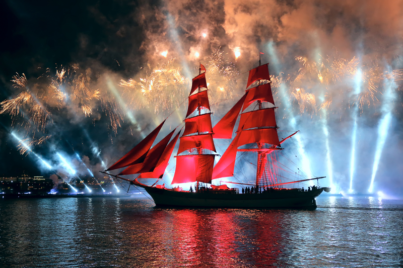Ship with red sails and white rays of light rising from the sea behind the ship at the White Nights Festival.