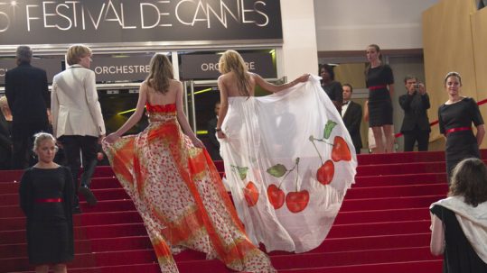 Two women in beautiful long ball gowns walking up the red-carpet stairs at the Cannes Film Festival.