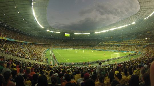 Soccer match being played, surrounded by a full stadium with an open dome at the FIFA World Cup.