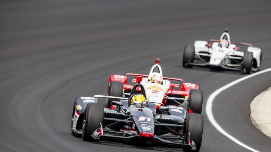 Three Indy race cars driving around the curve at the Indianapolis 500.