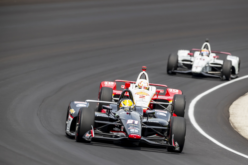 Three Indy race cars driving around the curve at the Indianapolis 500.