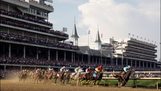 Thoroughbreds racing around the curve in front of the grandstand on the dirt track at the Kentucky Derby.