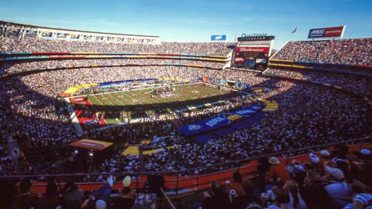 Football stadium with a sellout crowd watching the Super Bowl on a sunny day.
