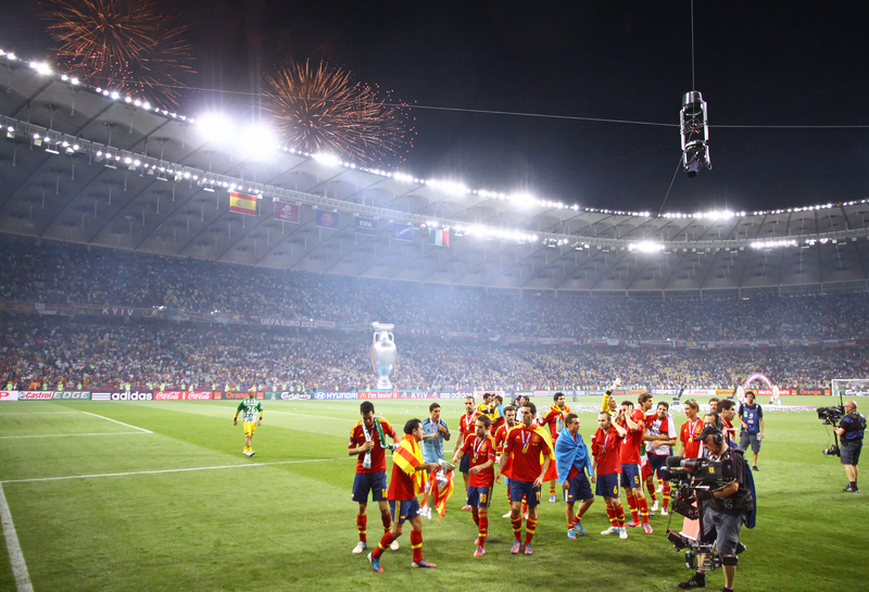 Soccer team celebrating their victory on the field in front of a full stadium and fireworks at night at the UEFA Euro Cup.