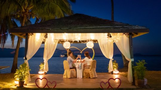 Couple having a romantic dinner under a canopy on the beach on Valentine's Day.