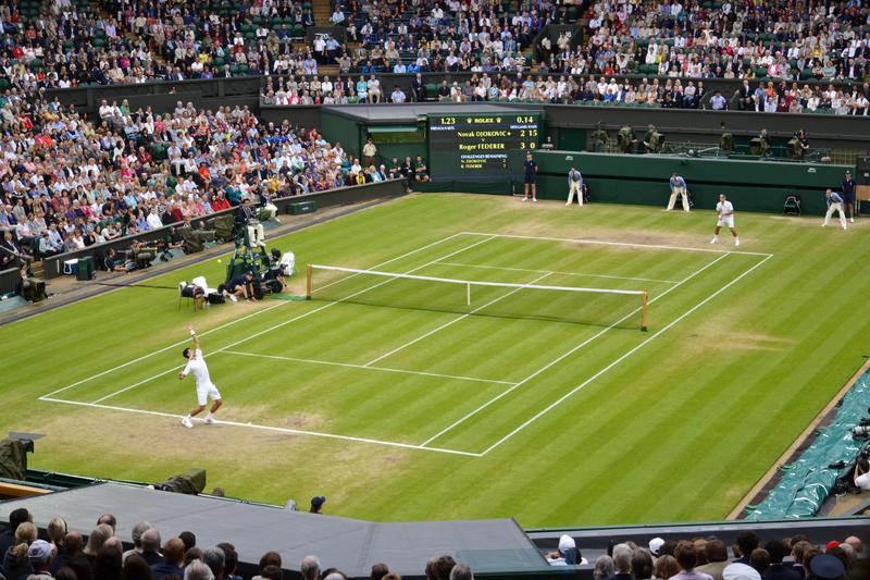 Tennis player serving during a match on the grass court at Wimbledon in front of a full stadium.