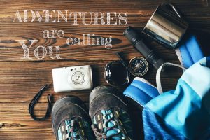 Accessories, backpack, shoes and utensils for hiking next to Inspirational and motivational quote: 'Adventures are calling you'.