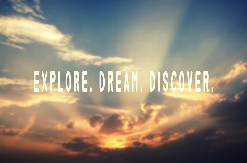 Inspirational travel quote 'Explore. Dream. Discover.' on beautiful sky with sun shining through the clouds.