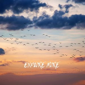 Inspirational exploration quote 'Explore more' on sunset sky background with large flock of birds exploring the skies and flying into the distance.