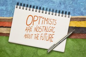 'Optimists are nostalgic about the future' quote in orange handwriting on a sketchbook against colorful abstract landscape.