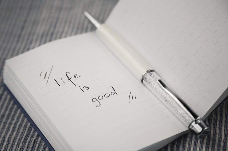 White notebook with 'Life is Good' inspirational quote written inside to remind you about living the good life.