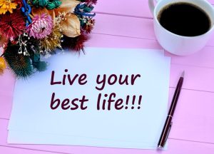 'Live your best life.' quote about living the good life on paper next to pen, flowers, and cup of coffee.