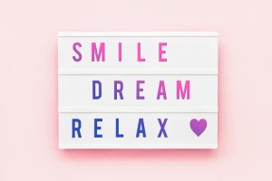 'SMILE DREAM RELAX' quote written in light box on pink background.