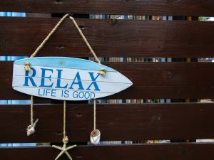 'Life is good.' motivational quote on a small surfboard sign with seashells hanging on a wooden fence at beach.