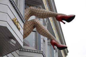 Giant legs in fishnet stockings and high heels posing out of a store window.