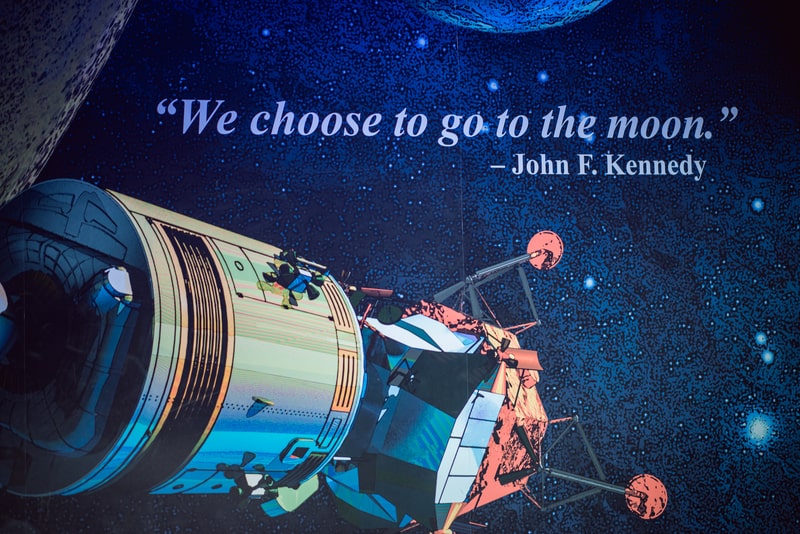 'We choose to go to the moon' space quote by John F Kennedy on sign with orbiter and starry space background at NASA Kennedy Space Center.