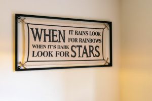 Minimalistic canvas held by a metal frame with inspirational motivational quote saying 'When It Rains Look For Rainbows When Its Dark Look For Stars.'