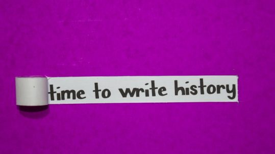 'Time to write history' quote about time written in market on white tape roll stuck to a purple wall.
