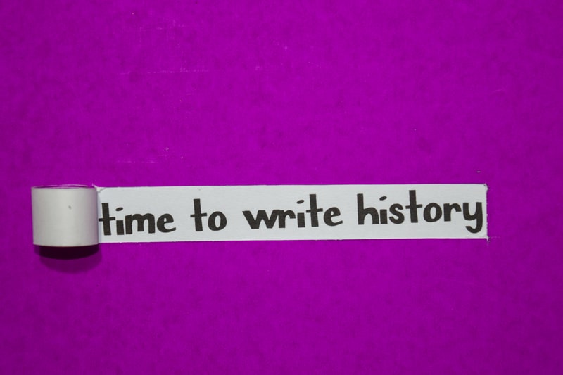 'Time to write history' quote about time written in market on white tape roll stuck to a purple wall.