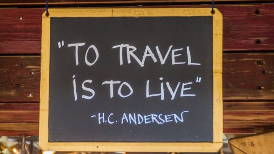 Hans Christian Anderson inspirational quote on chalkboard saying 'To travel is to live'