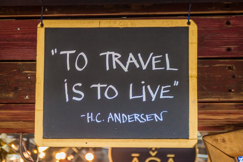 Hans Christian Anderson inspirational quote on chalkboard saying 'To travel is to live'