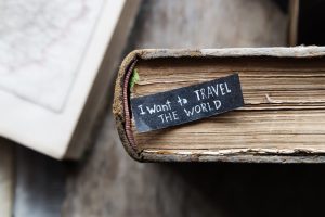 'I want to travel the world' quote inscribed on a label on an old book next to maps
